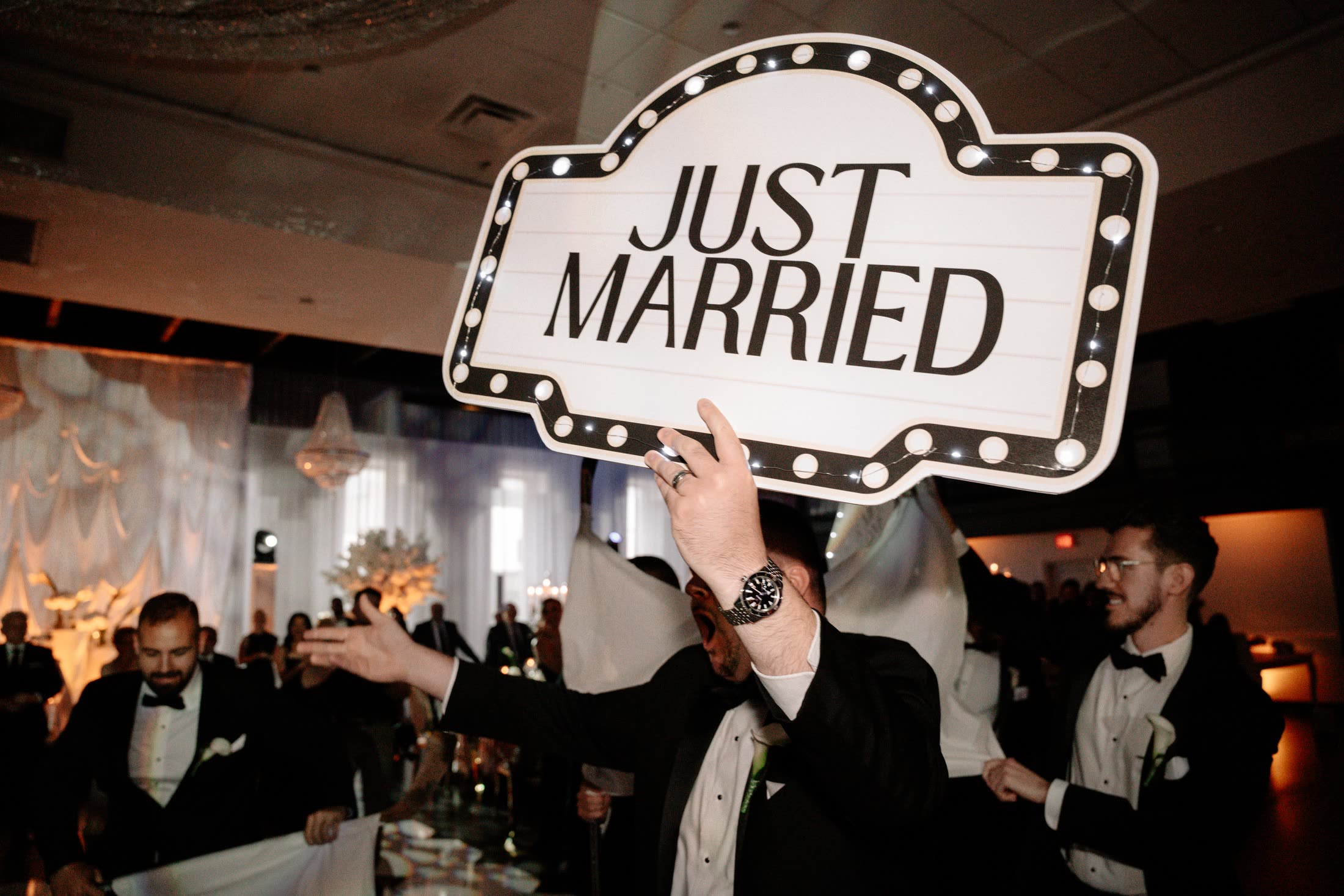 Groomsman holding a lit Just Married sign above a packed reception