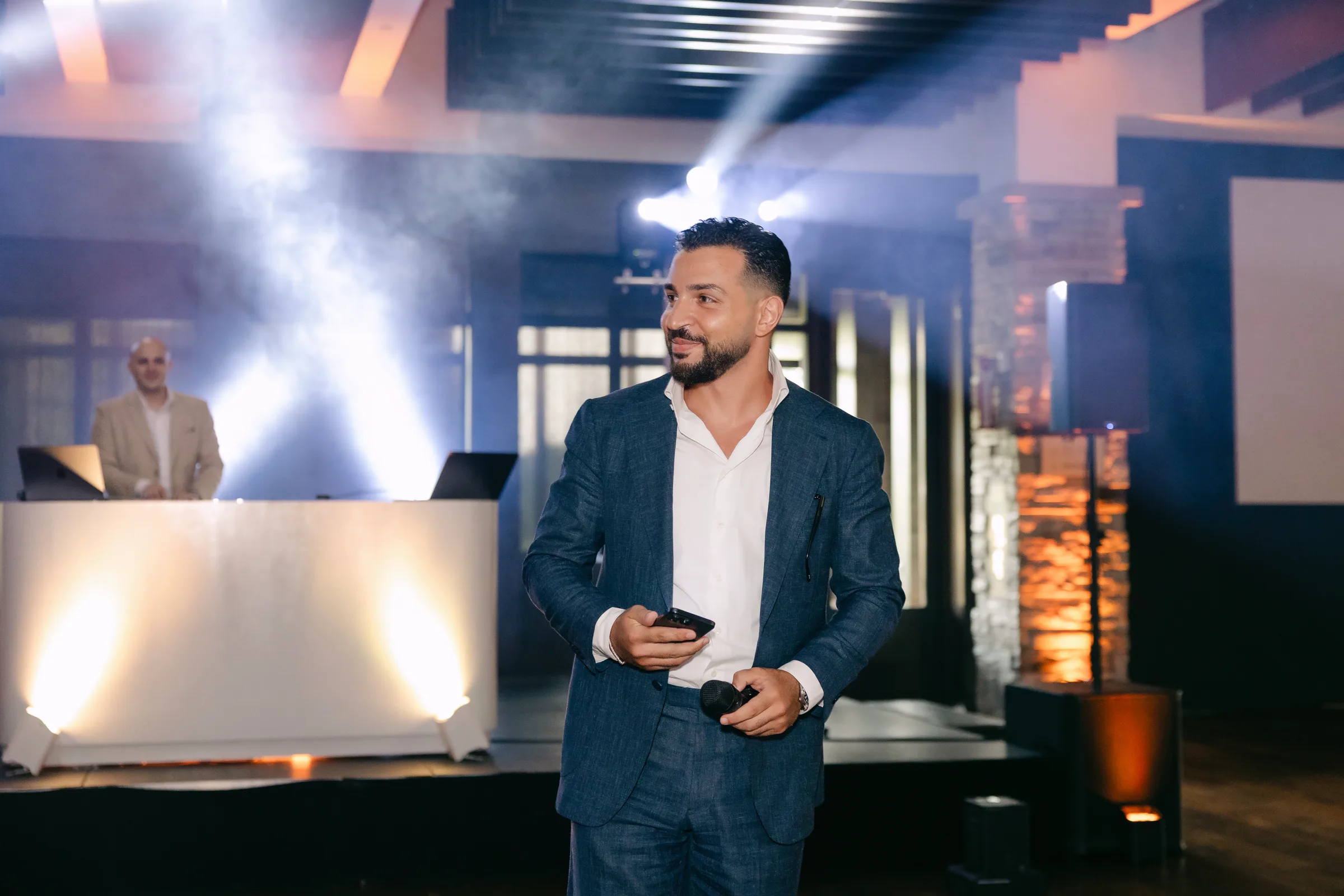 Majd en blazer bleu tenant le micro, la console et les faisceaux derrière lui